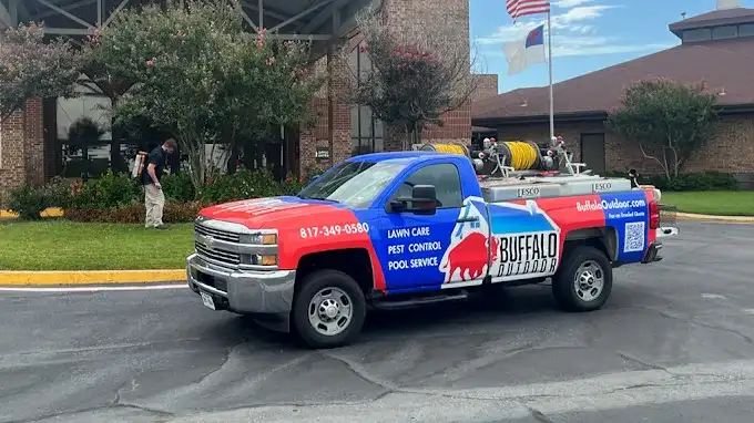 Buffalo Outdoor truck, wrapped with the phone number and logo, parked at a job with a technician treating the grounds behind it