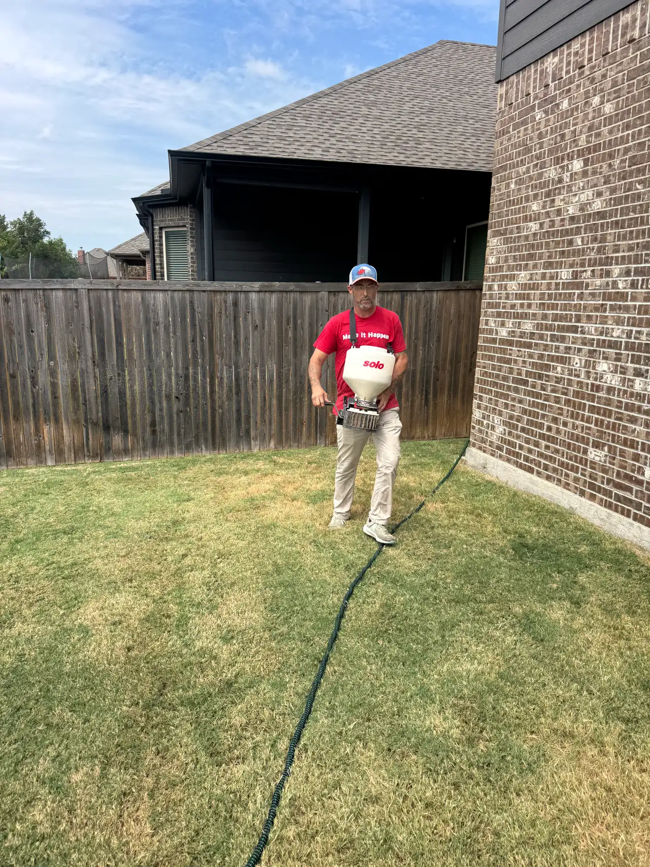 Buffalo Outdoor technician broadcasting granular fire ant bait across a lawn with a chest spreader