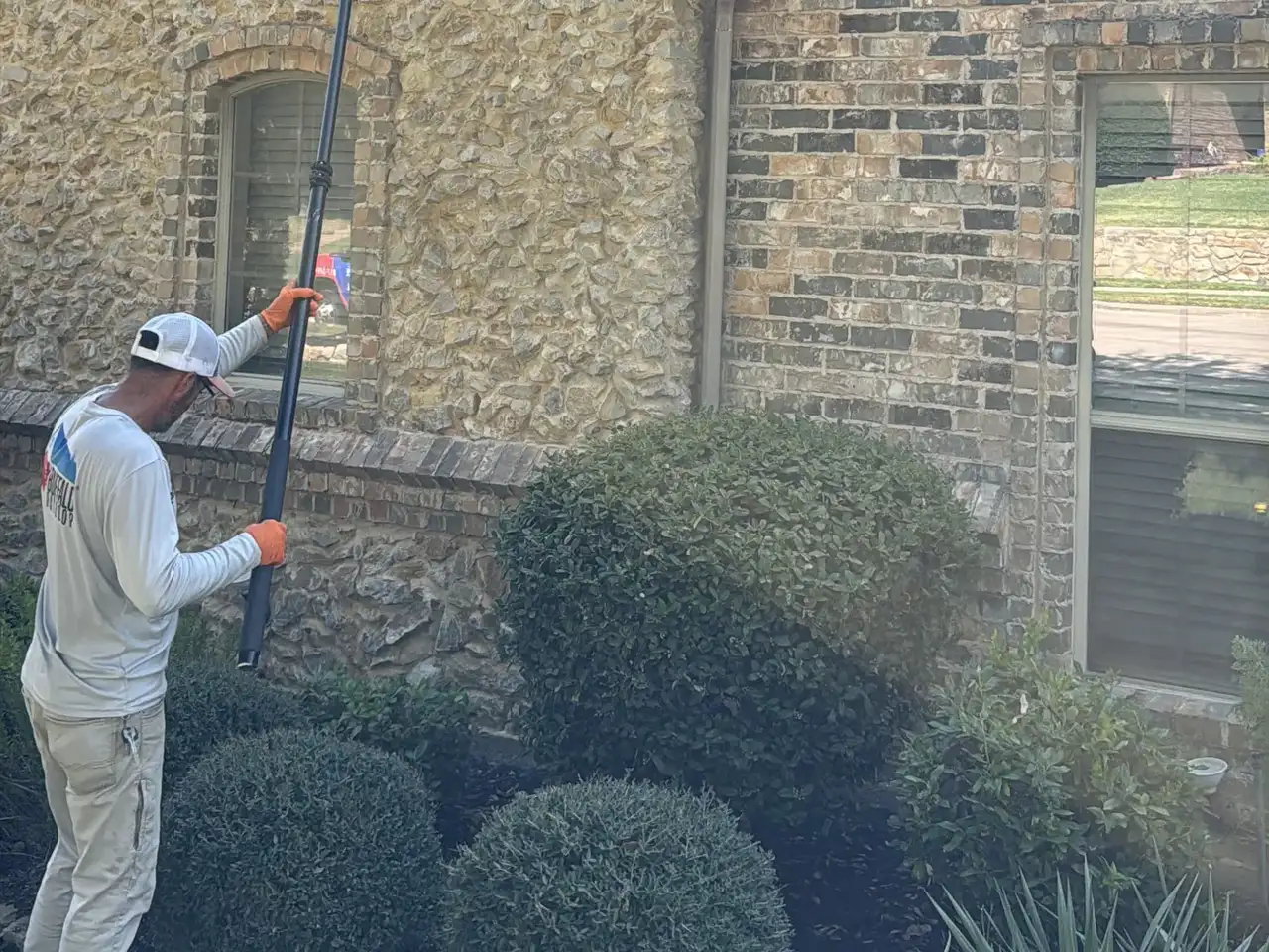 Buffalo Outdoor technician in long sleeves and gloves clearing spider webs from the eaves with an extended web pole
