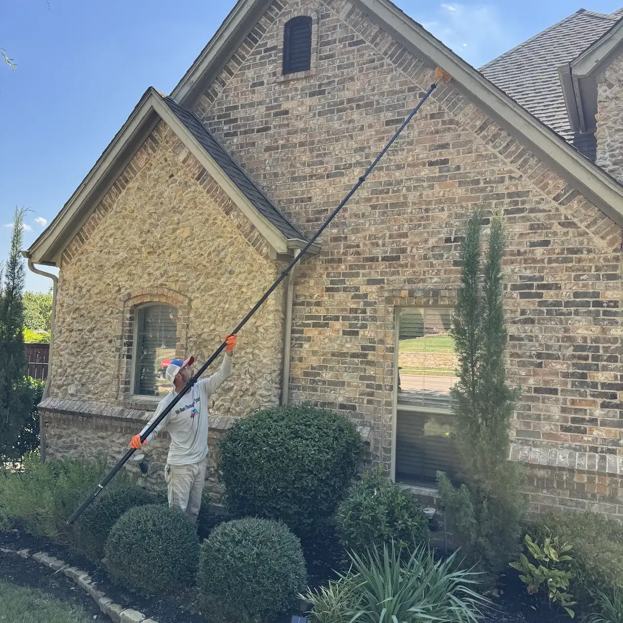 Buffalo Outdoor technician in long sleeves and gloves reaching the roofline eaves with an extended web pole