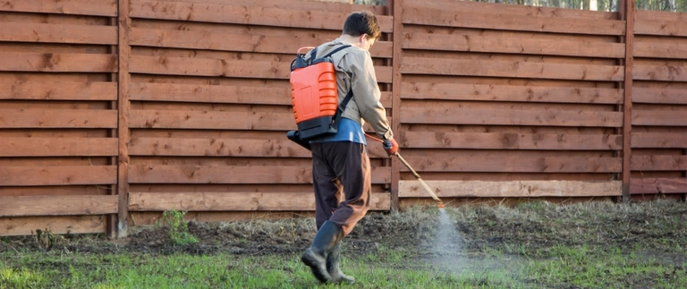 Buffalo Outdoor technician walking a fence line with a backpack sprayer
